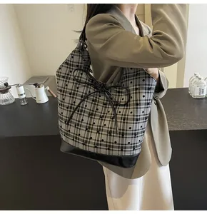 Detail shot of a large grey plaid tote bag with a big black bow carried by a model
