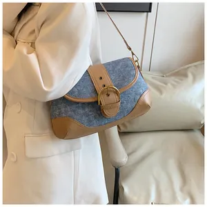 Detail view of denim and brown leather patchwork shoulder bag with golden buckle