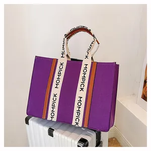 Macro view of purple felt tote bag with lettered handles on a silver suitcase