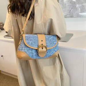 Retro denim underarm bag with brown leather trim and metal buckle on trench coat model