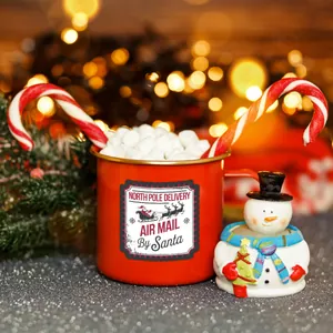 Detail einer roten Weihnachts-Emailletasse mit Nordpol-Poststempel und Marshmallows