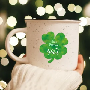 Gros plan d'un mug vintage en céramique avec trèfle tenu par une personne en pull blanc