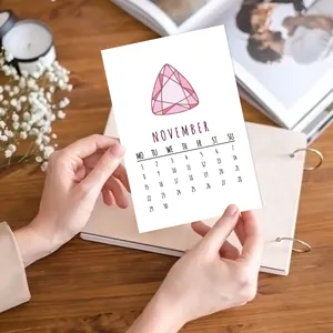 Detailed November calendar card with pink gemstone illustration held over a wooden desk
