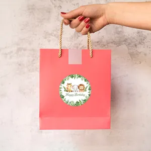 Pink birthday gift bag with cute animal sticker and golden handles held by hand