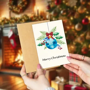 Close-up of a watercolor Christmas card with envelope held against a warm fireplace