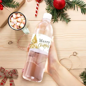 Hand die waterfles vasthoudt met Merry Christmas-label en gouden kerstboomontwerp