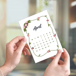 Hands holding a 2026 April calendar card with floral borders for wall decoration