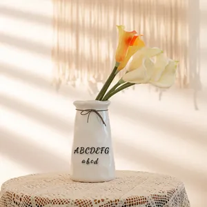 Off-white ceramic vase with letter prints and calla lily flowers on lace tablecloth