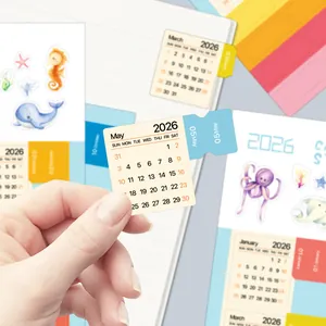Primo piano degli adesivi per calendario 2026 con linguette blu su carta minimalista