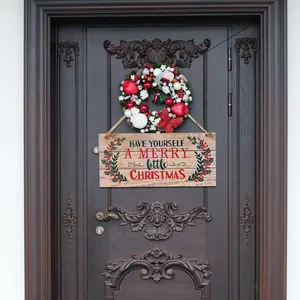Detail eines Weihnachtsholzschilds an dunkler Tür mit festlichem Kranz und Botschaft
