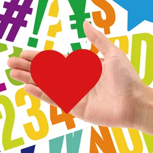 Close-up of red heart stickers held by hand with colorful alphabet background