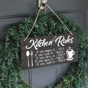 Dettaglio di una targa in legno Kitchen Rules appesa a una ghirlanda verde