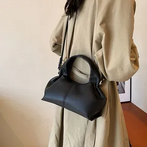 Minimalist black leather dumpling handbag with crossbody strap and gold metal accents
