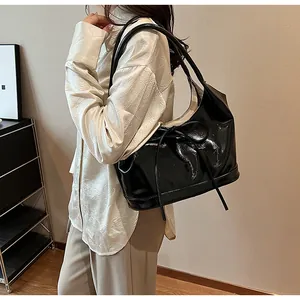 Glossy black patent leather shoulder bag with bow detail shown on a model's arm
