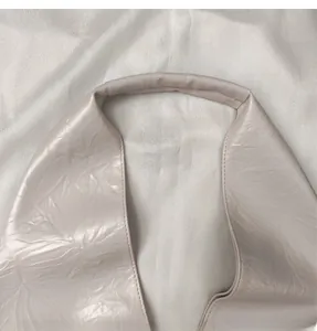 Close-up of cream soft leather underarm bag featuring elegant pleated texture and wide strap