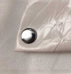 Detailed close-up of a silver metal rivet on beige pleated faux leather handbag