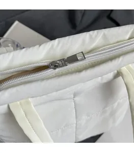 Detail of white quilted nylon tote bag featuring silver zipper and cream shoulder strap