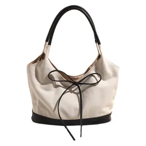 Minimalist canvas tote bag with black leather bow detail and shoulder strap contrast