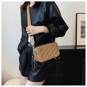 Detail of khaki crossbody bag featuring quilted semi-circle patterns and tassel charm