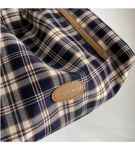 Detail view of woven plaid fabric and leather brand tag on large canvas tote bag