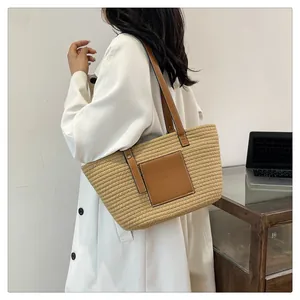 Close-up of woven straw tote bag with brown leather shoulder straps and pocket detail