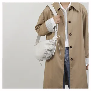 Minimalist white drawstring crossbody bag showing side view on a beige trench coat