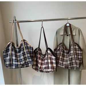 Three color variants of large plaid canvas tote bags with leather straps hanging on a rack