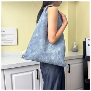 Side view of large washed denim blue tote bag with metallic rivet details on wide strap