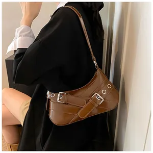 Brown leather underarm bag with silver metal eyelets shown on a model in a black coat