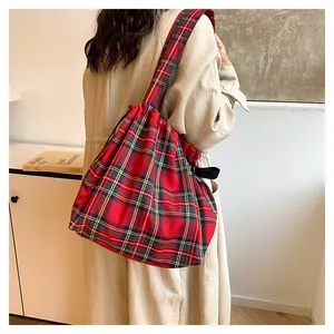 Close-up of red plaid drawstring bucket bag with wide shoulder strap on a person
