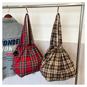 Detail view of two plaid canvas tote bags with drawstring closure hanging on a metal rack
