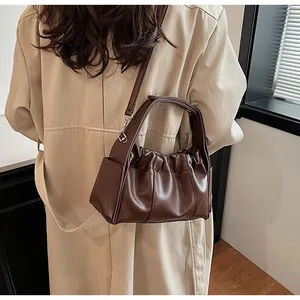 Detailweergave van de donkerbruine geplooide emmertas gedragen bij een beige trenchcoat
