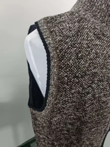 Detail of knitted vest shoulder and armhole with black ribbed binding on mottled fabric