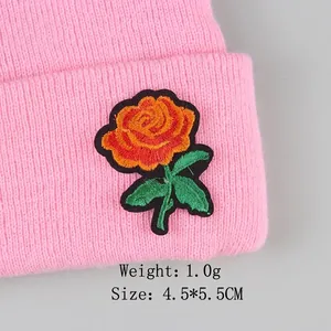 Rose embroidery patch on a pink knitted beanie with green leaves and black border detail