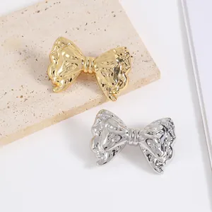 Bow-shaped metal brooch with hammered texture in gold and silver finish on stone