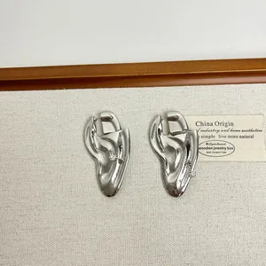 Detailed close-up of silver-tone biomimetic ear studs with liquid metal texture and stones