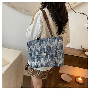 Detail of blue-grey woven tweed tote bag with brown leather shoulder strap and metal logo