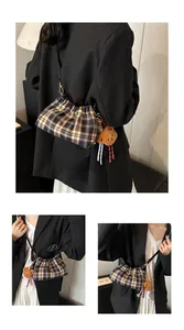 Detalle de bolso cubo plisado a cuadros con colgante de oso y herrajes dorados