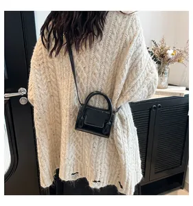 Close-up of a black patent leather mini square bag worn over a beige knitted sweater