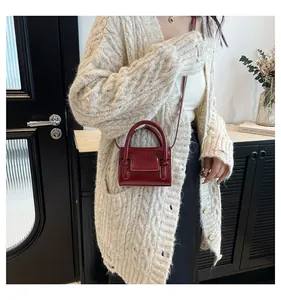 Close-up of a burgundy glossy mini handbag worn with a chic knit cardigan and dark skirt