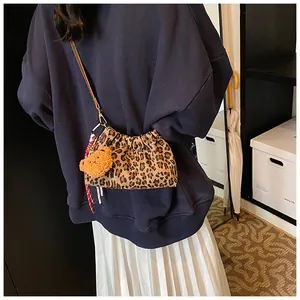 Detalle de bolso tipo cubo de leopardo con colgante de oso amarillo y cinta roja tejida
