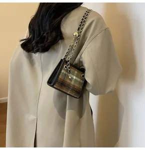 Detail of green plaid tweed shoulder bag with gold chain strap worn over trench coat