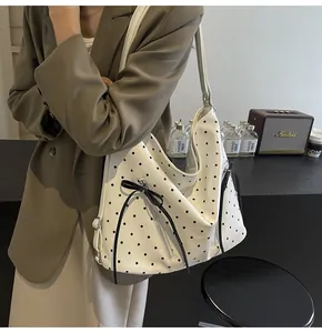 Close-up of white polka dot tote bag featuring side zippers and black ribbon bow detail