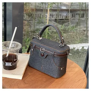 Detail of dark grey denim box bag with rivet pocket and brown leather trim on wooden table