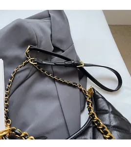 Détail de la bandoulière chaîne dorée réglable sur un sac matelassé noir et costume gris