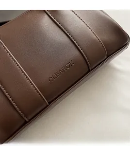 Detail shot of deep brown leather texture with vertical stitching and embossed logo
