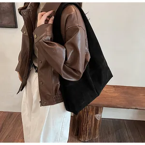 Close-up of a large black suede tote bag paired with a brown faux leather jacket