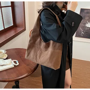 Brown suede tote bag shown on model wearing a black coat in a warm interior setting