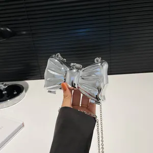 Primer plano de un bolso de lazo plateado en acrílico efecto espejo con asa de cadena