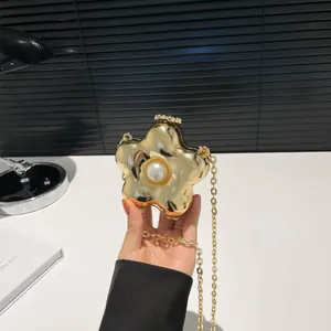 Detalle de bolso de fiesta dorado en forma de flor con perla central y cadena fina